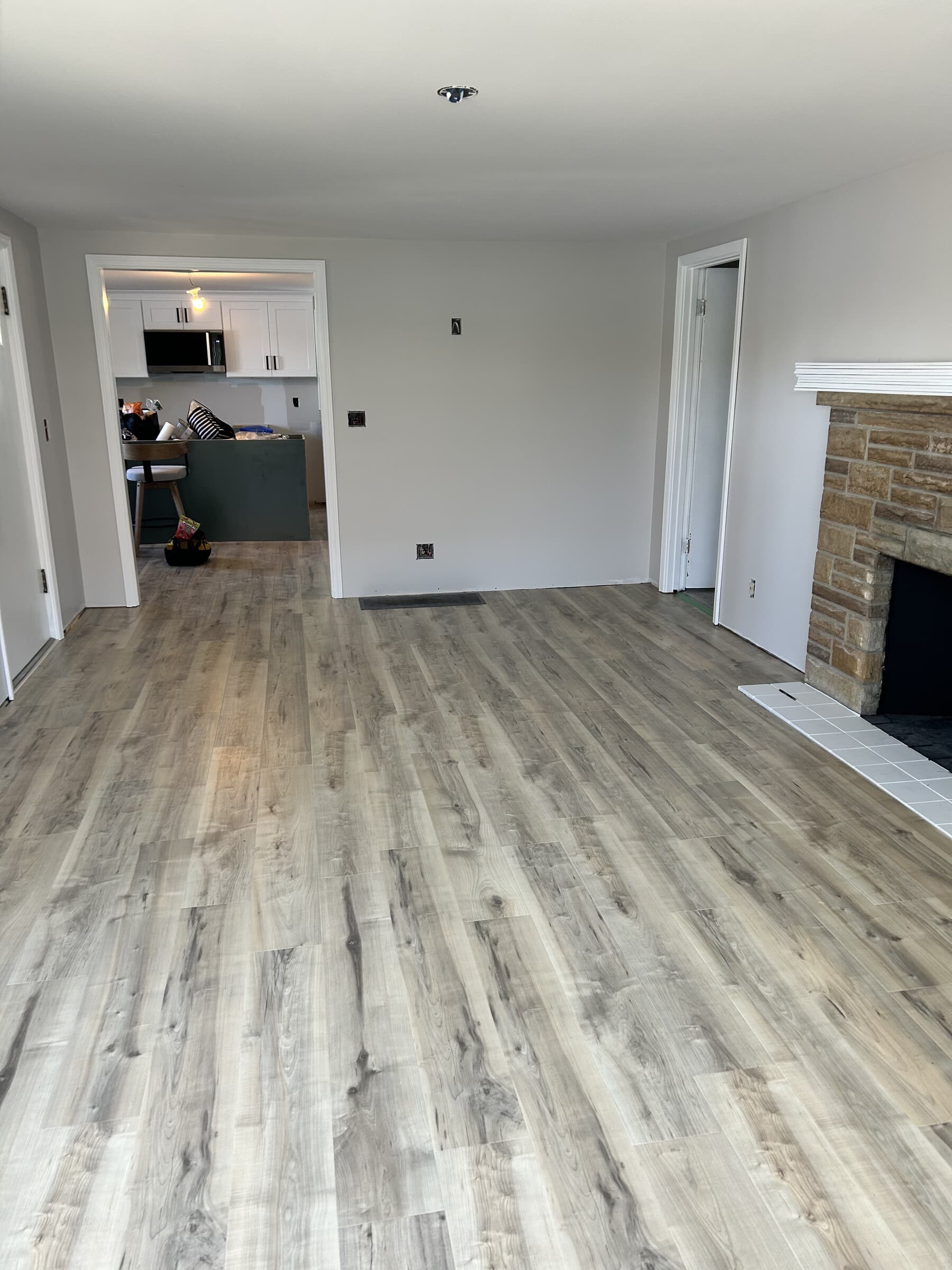 Open-plan living room with stone fireplace at right and archway to sage kitchen at left, wide-plank floors throughout